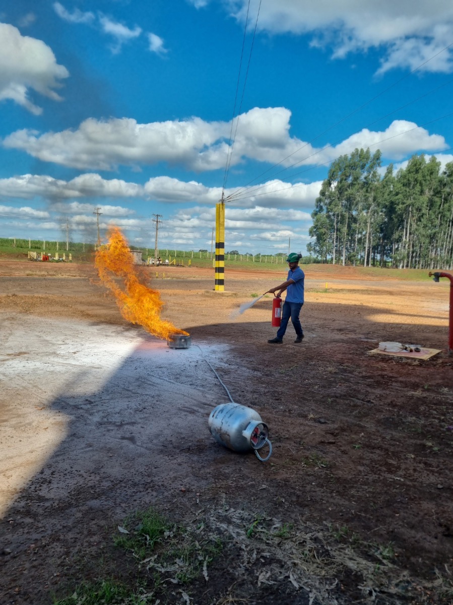 Treinamento de brigada de incêndio: participante combatendo fogo com extintor em campo a céu aberto